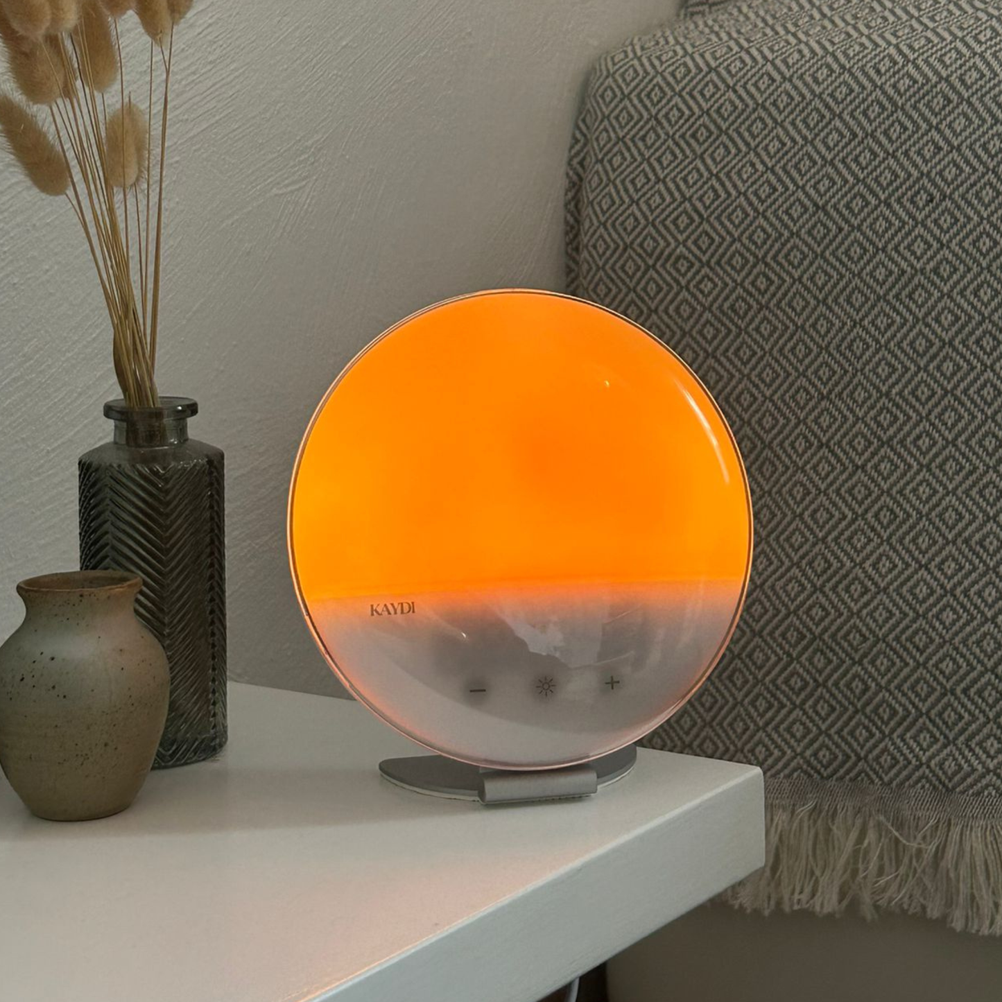 Kaydi One wake up lights displayed in a row on a windowsill, glowing in warm sunrise colors from yellow to red.