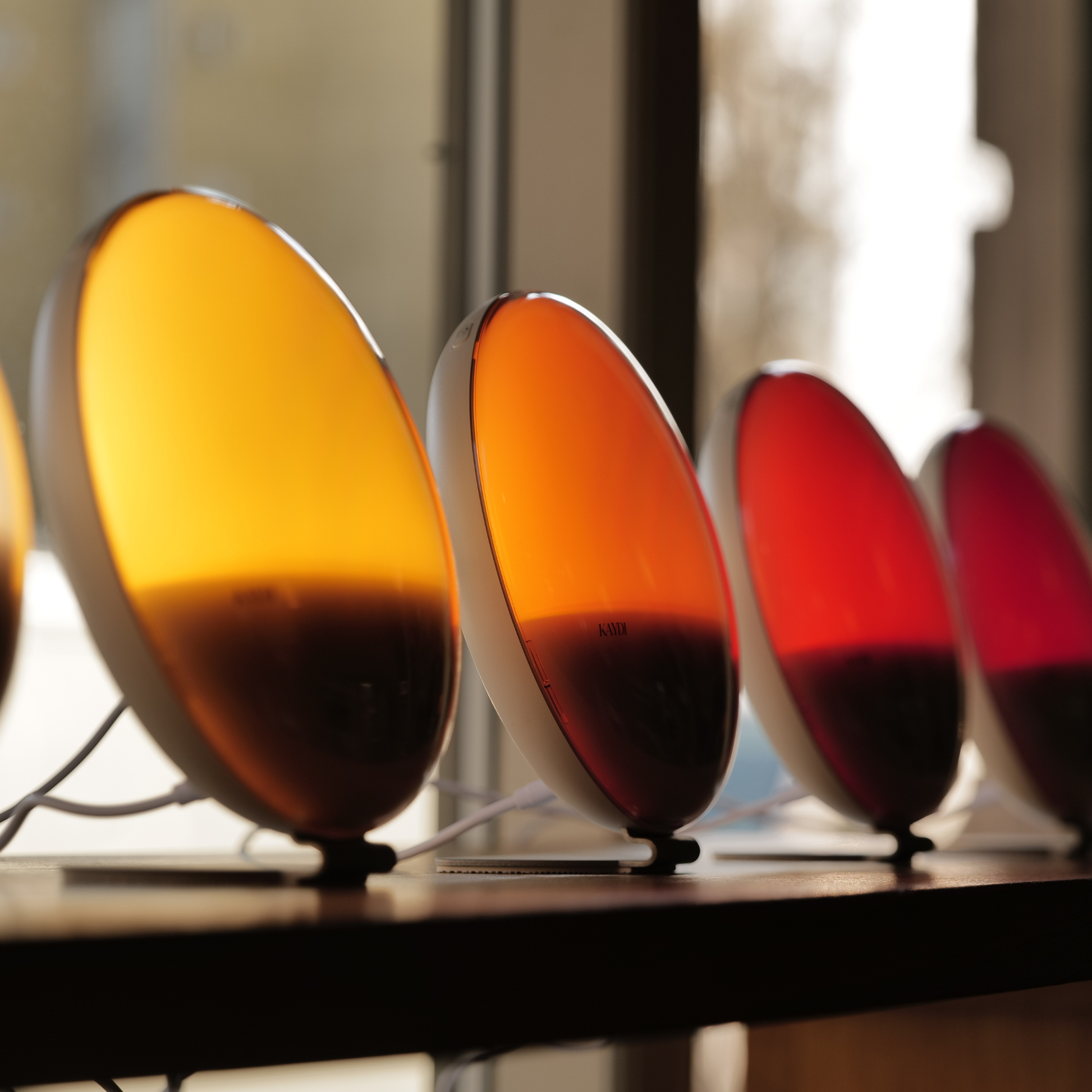 Kaydi One wake up lights lined up in a store window, showcasing the full color spectrum from soft white to deep red.