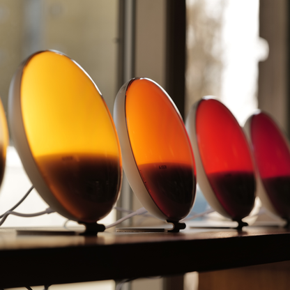 Kaydi One wake up lights lined up in a store window, showcasing the full color spectrum from soft white to deep red.