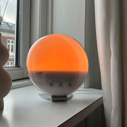 Kaydi wake up light glowing soft orange on a windowsill beside a curtain with daylight visible outside.