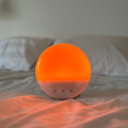 Kaydi wake up light glowing warm orange on a bed with soft white bedding in the background.